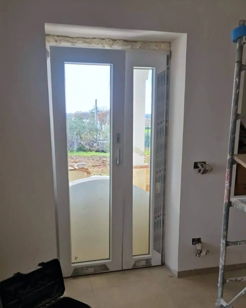 Porta in PVC bianco a due ante montata in una casa in ristrutturazione